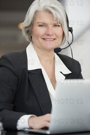 Smiling Businesswoman in headset typing on laptop