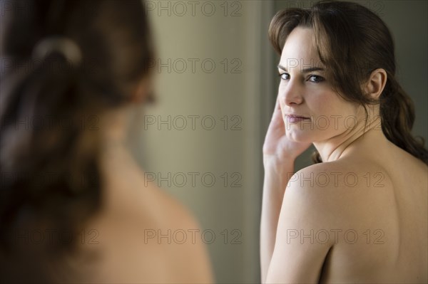 Nude Hispanic woman examining herself in mirror