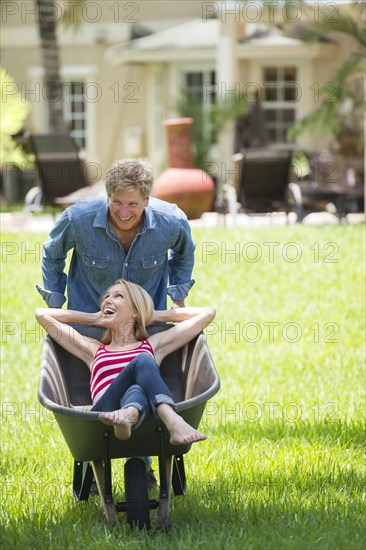 Caucasian man pushing girlfriend in wheelbarrow