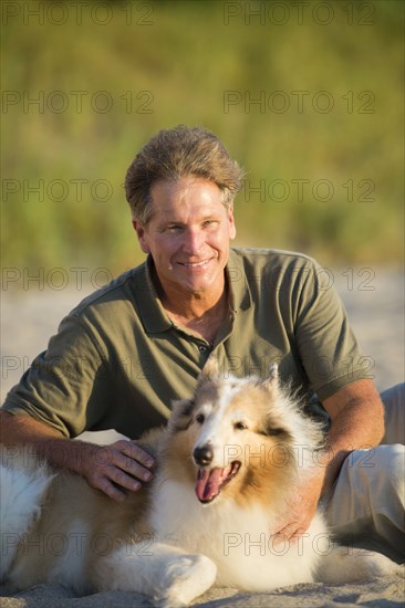 Caucasian man sitting with dog on beach