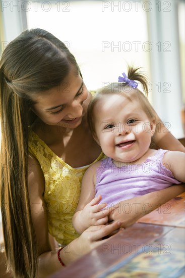 Hispanic girl holding toddler sister at table