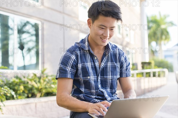 Korean man using laptop outside building