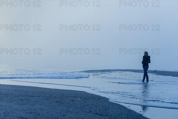 Caucasian woman walking in waves on beach