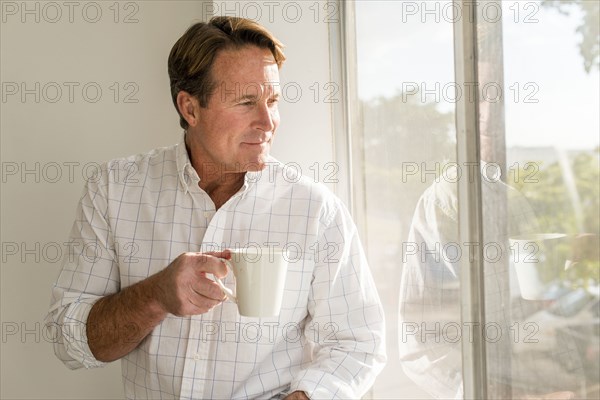 Caucasian man drinking cup of coffee near window