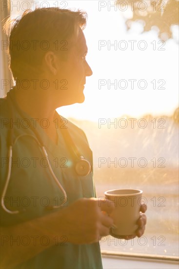 Caucasian nurse drinking cup of coffee at window