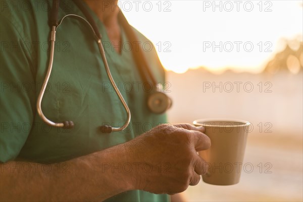 Caucasian nurse drinking cup of coffee at window