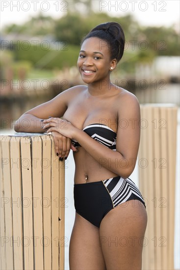 Mixed race woman wearing bikini leaning on post