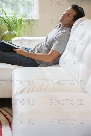 Hispanic man with digital tablet napping on sofa