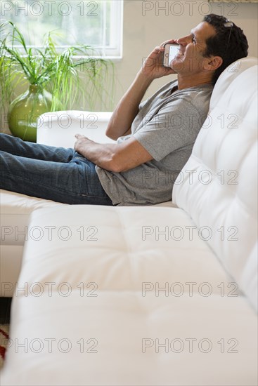 Hispanic man talking on cell phone on sofa