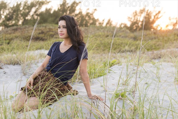 Hispanic woman sitting on sand dunes