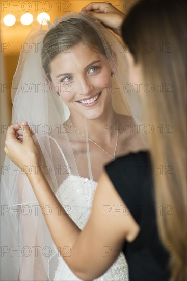 Caucasian bridesmaid arranging veil for bride