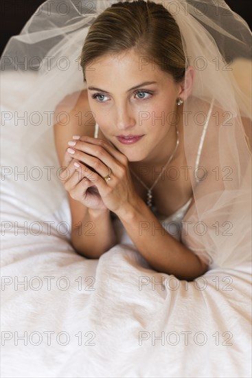 Caucasian bride in wedding veil laying on bed