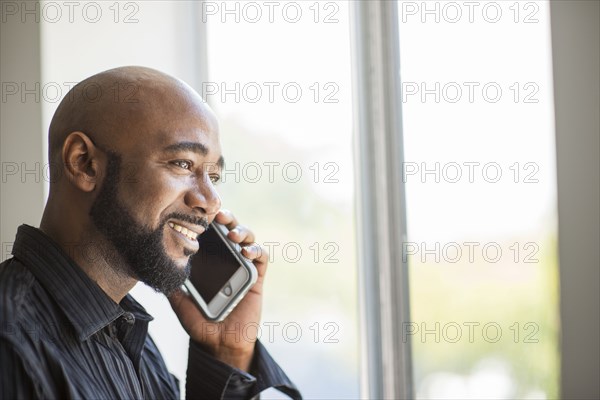 Black man talking on cell phone near window