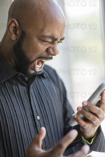 Frustrated black man using cell phone near window