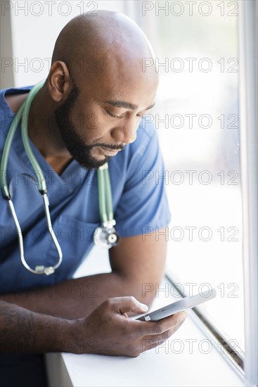 Black nurse using cell phone near window