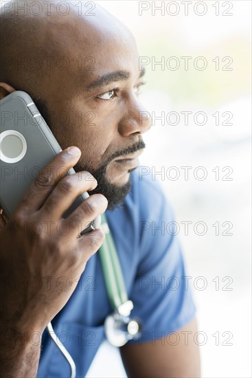 Black nurse talking on cell phone near window