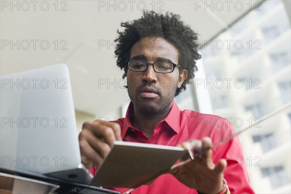 Hispanic businessman writing notes at glass office desk
