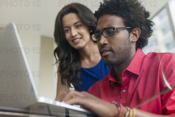 Hispanic business people using laptop at glass office desk