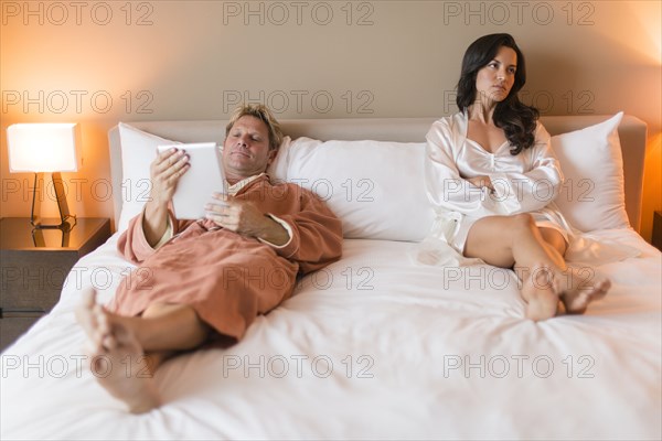 Man with digital tablet ignoring girlfriend in bed