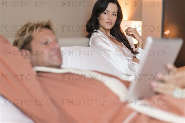 Man with digital tablet ignoring girlfriend in bed