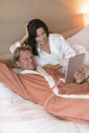 Couple using digital tablet on bed