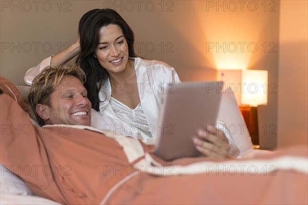 Couple using digital tablet on bed