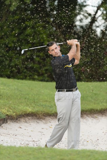 Caucasian man chipping from golf course sand trap