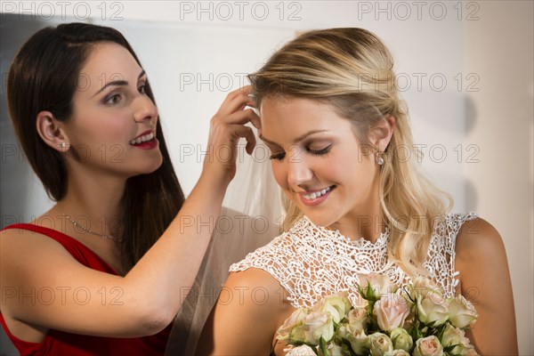 Bridesmaid adjusting veil of bride before wedding