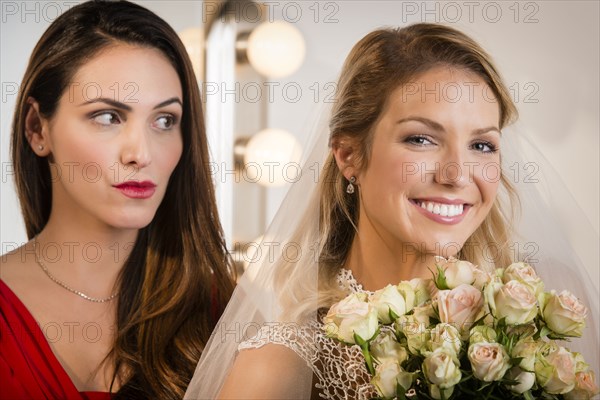 Suspicious bridesmaid standing behind smiling bride