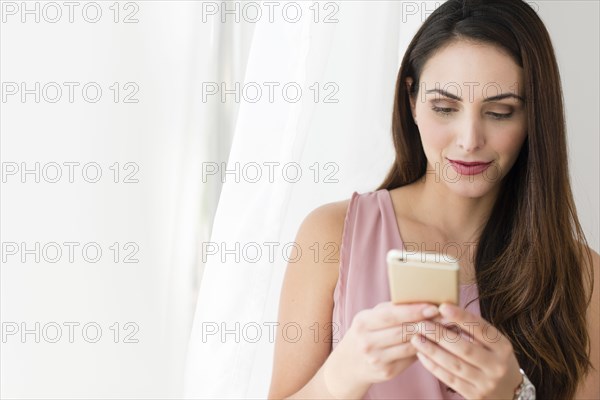 Businesswoman using cell phone near curtain