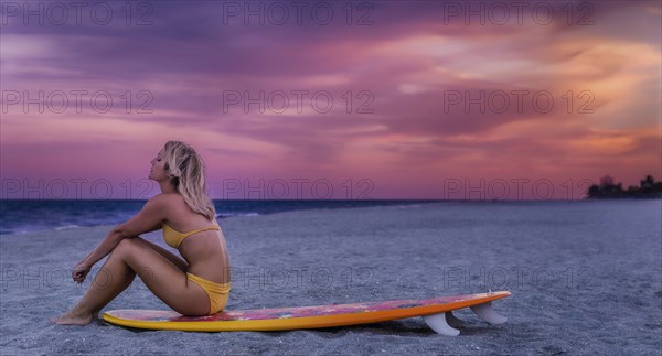 Caucasian woman sitting on surfboard on beach