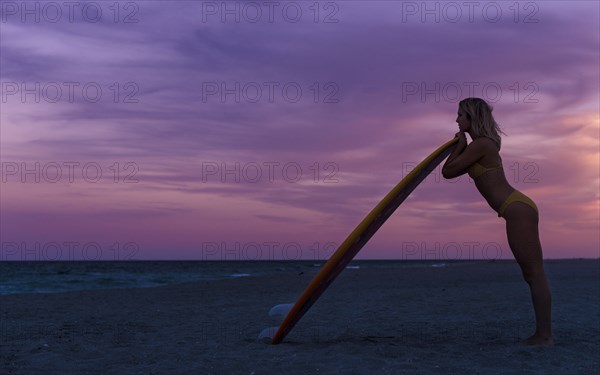 Caucasian woman leaning on surfboard on beach