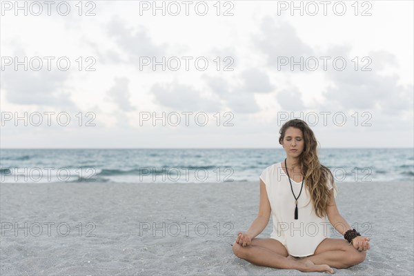 Hispanic woman meditating on beach