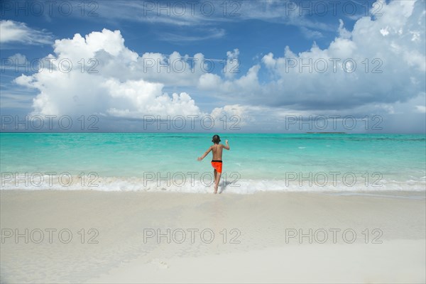 Hispanic boy running in waves on beach