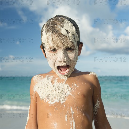 Hispanic boy covered in sand on beach