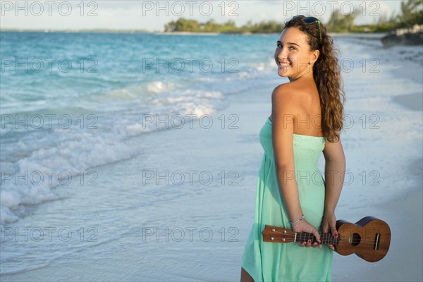 Hispanic teenage girl holding ukulele on beach