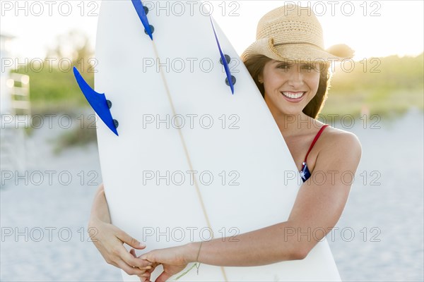 Hispanic woman carrying surfboard on beach