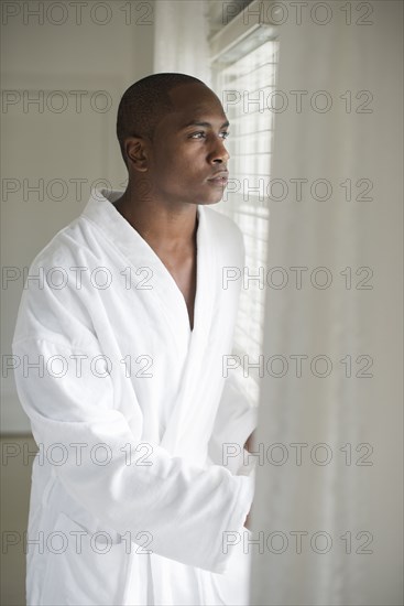 Black man in bathrobe looking out window