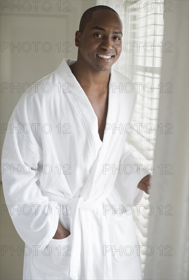 Black man in bathrobe standing at window