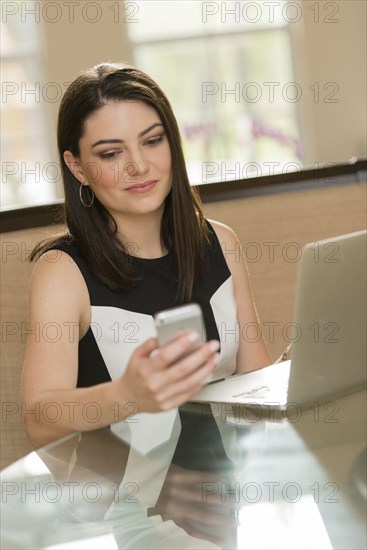 Hispanic businesswoman using cell phone in office