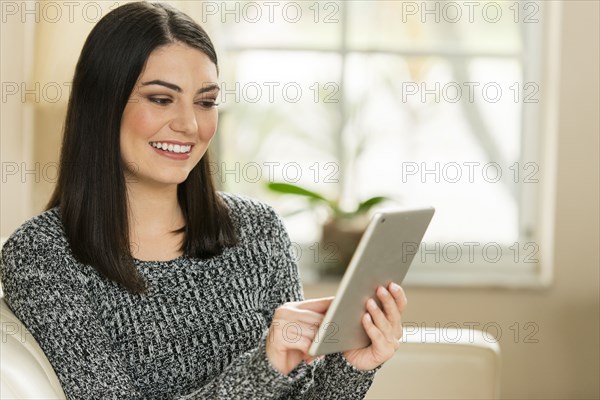 Hispanic woman using digital tablet on sofa