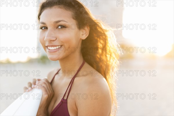Mixed race teenage girl carrying surfboard on beach