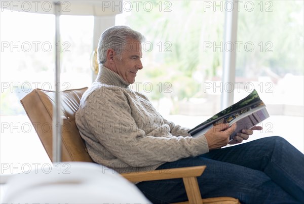 Caucasian man reading magazine in armchair