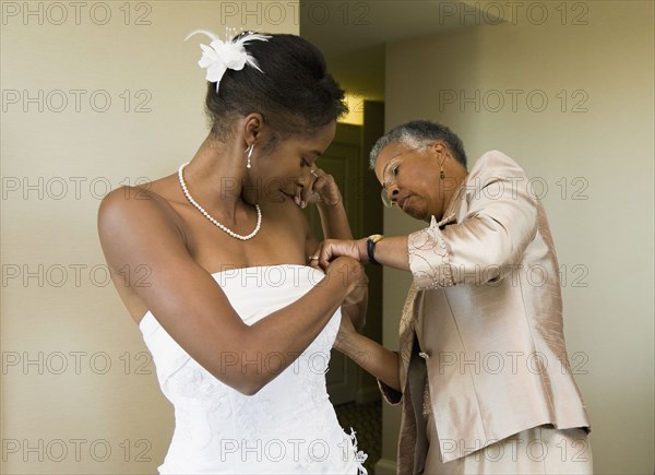 African mother helping bride with wedding dress