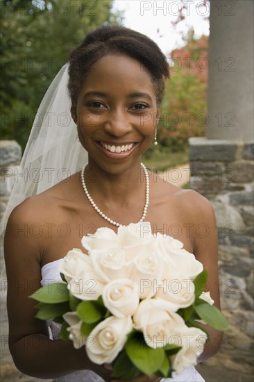 African bride holding rose bouquet and smiling