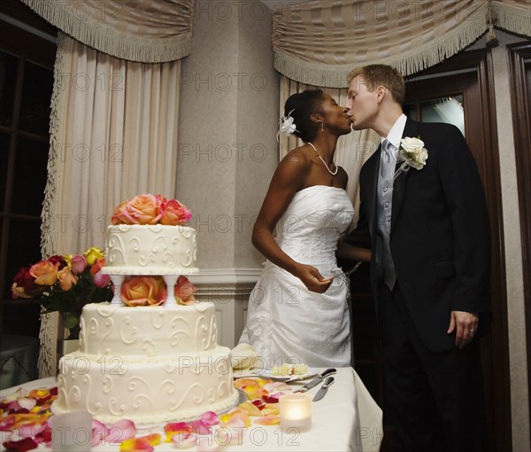 Bride and groom kissing next to wedding cake