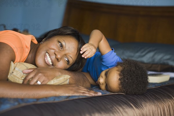 African mother laying on bed with young son