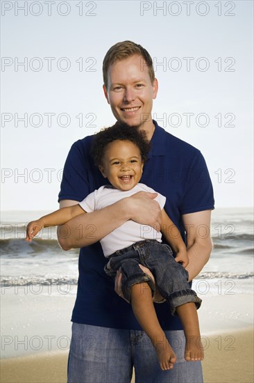 Father holding mixed race son at beach