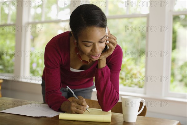 African woman writing and talking on cell phone