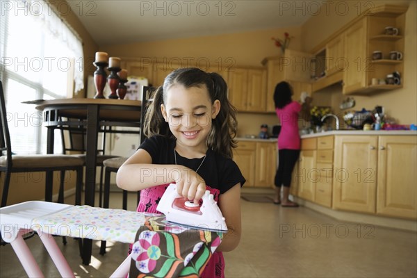 Girl using toy iron and ironing board in kitchen